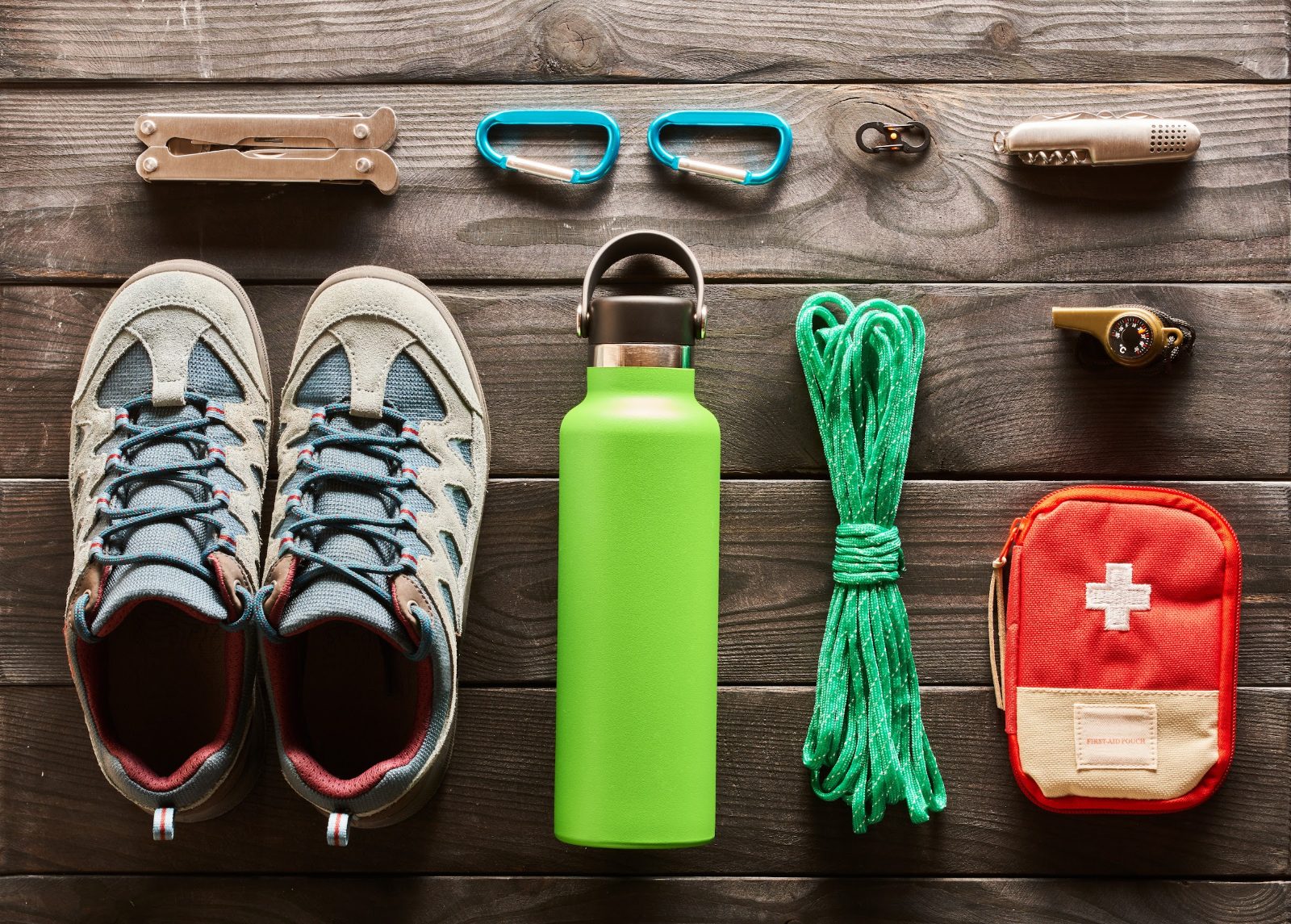 Day hike gear flat lay with trail shoes, water bottle, first aid kit and multitool