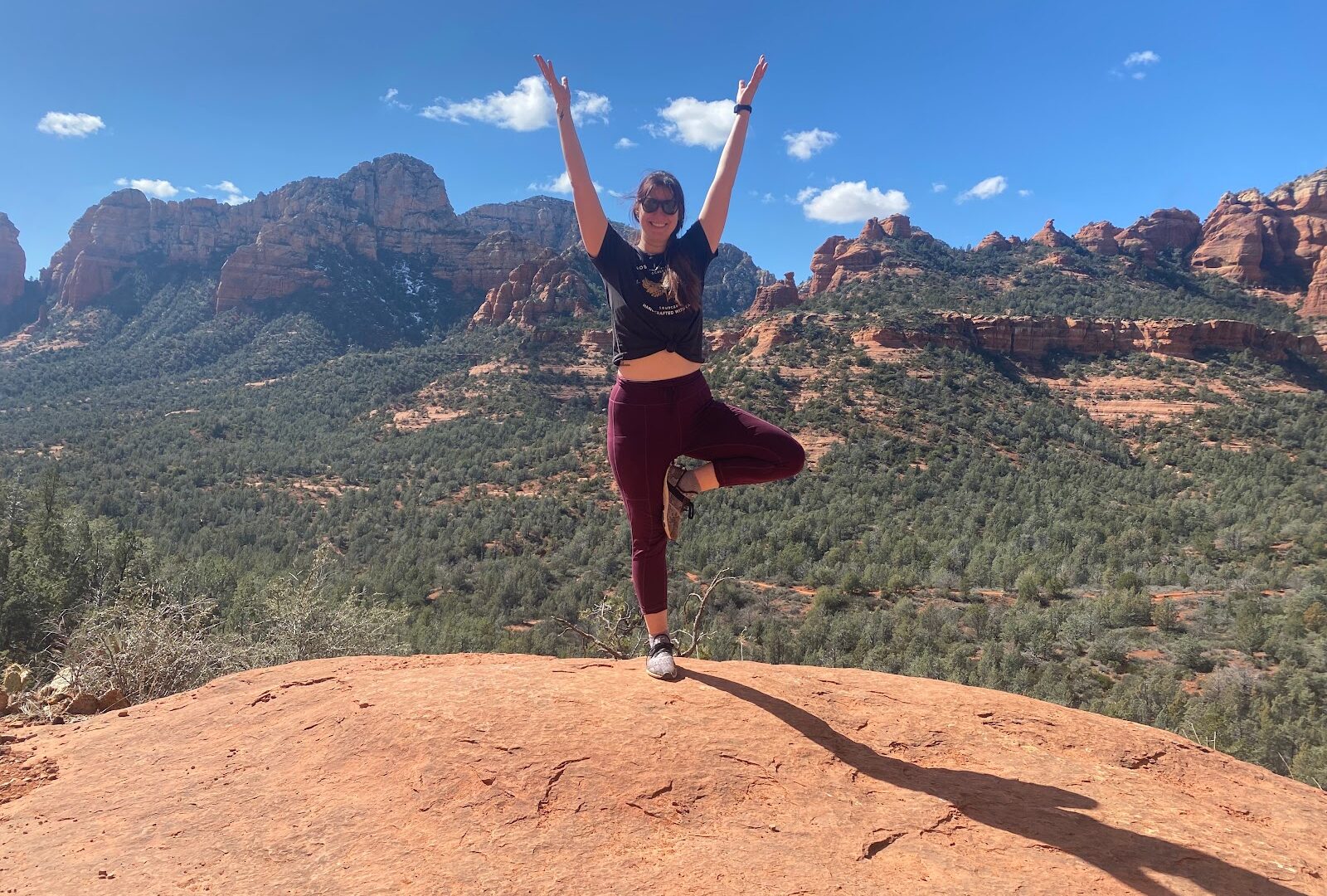 Woman in tree pose on a red rock ledge overlooking Sedona during the Sedona Yoga Festival season