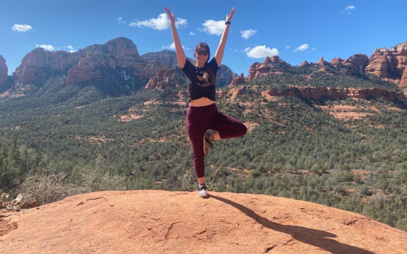 Woman in tree pose on a red rock ledge overlooking Sedona during the Sedona Yoga Festival season