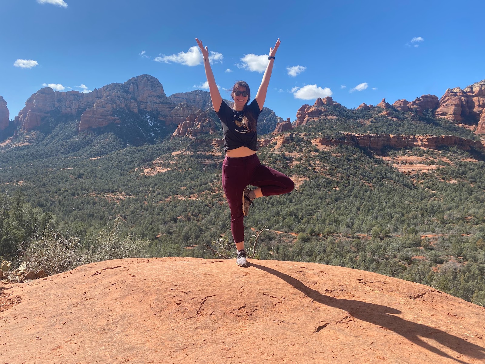 Woman in tree pose on a red rock ledge overlooking Sedona during the Sedona Yoga Festival season