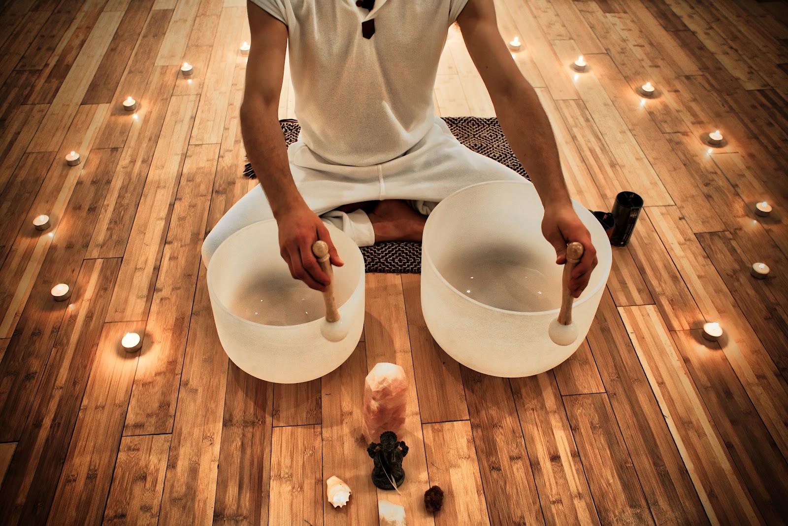 A sound healing practitioner playing crystal singing bowls by candlelight